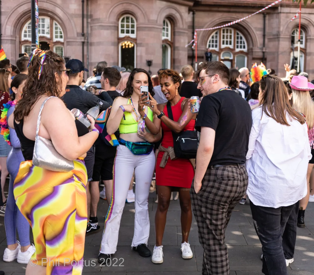 A group of people at an outdoor event are taking a selfie with a smartphone.