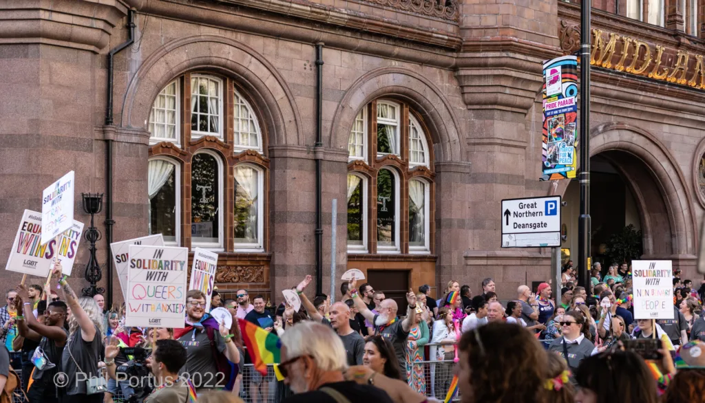 A large crowd gathers outside a grand building with arched windows and ornate details.