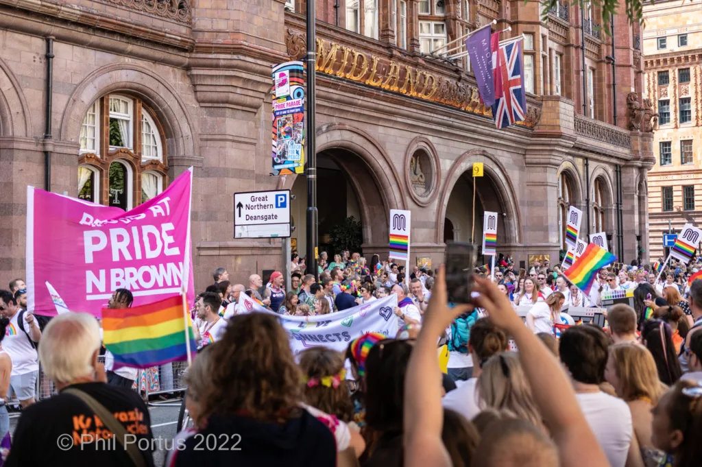 A large crowd gathers on a sunny day in front of a grand stone building with flags and banners.