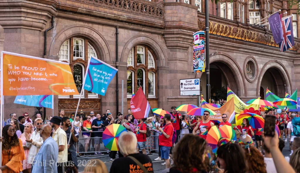 A crowd gathers on a city street during an event with colorful umbrellas and banners.