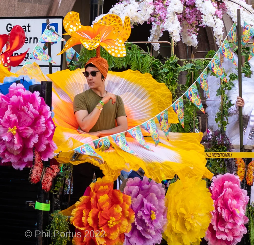 A person holding yellow fans stands amidst vibrant artificial flowers and colorful banners.