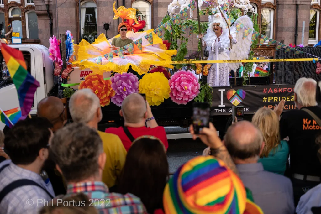 A parade float decorated with large paper flowers and streamers moves past a crowd of onlookers.