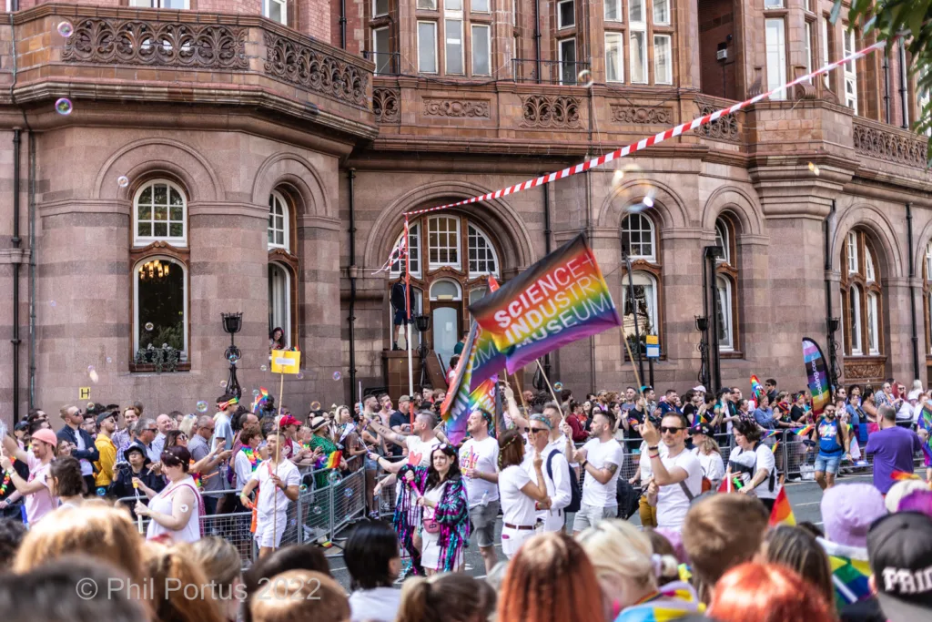 A large crowd gathers for an outdoor event in front of a grand building with multiple windows.