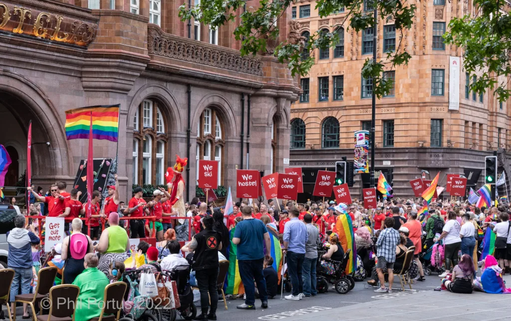 A large crowd gathers along a street during an event with flags and signs visible.