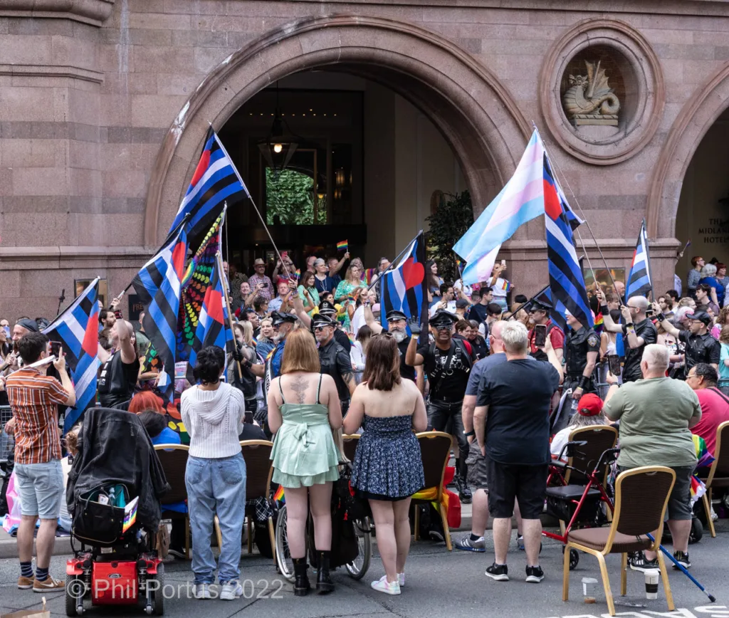 A large crowd gathers outdoors with numerous flags being held aloft.