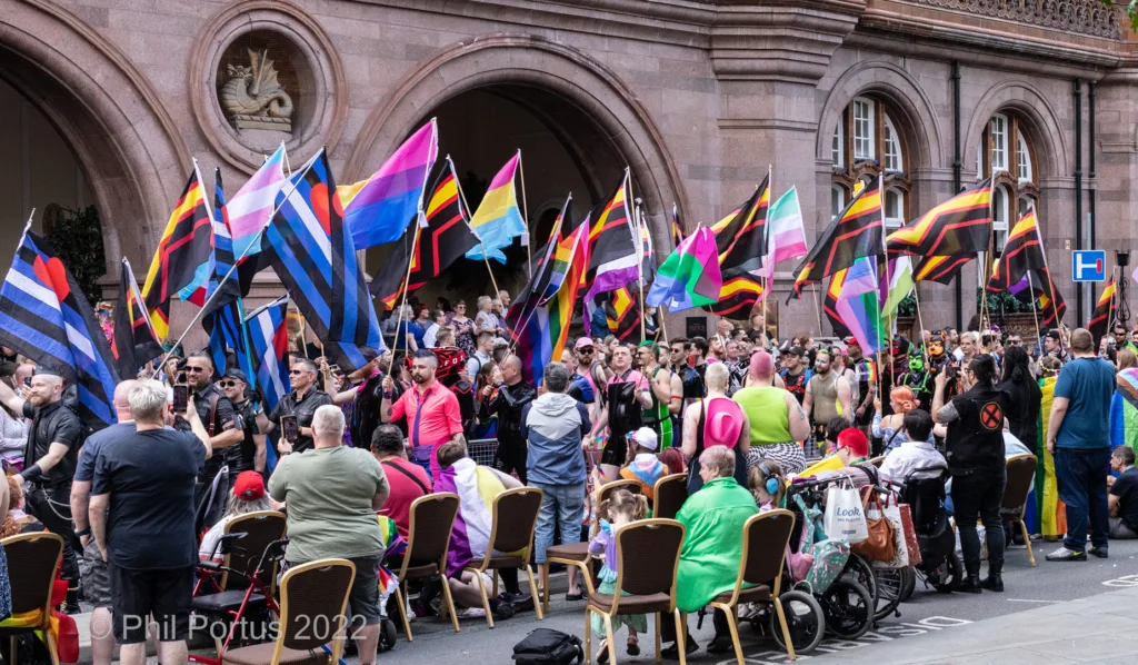 A large crowd gathers outdoors with numerous colorful flags visible among the people.