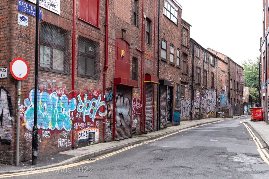 A narrow street lined with brick buildings is covered in colorful graffiti.