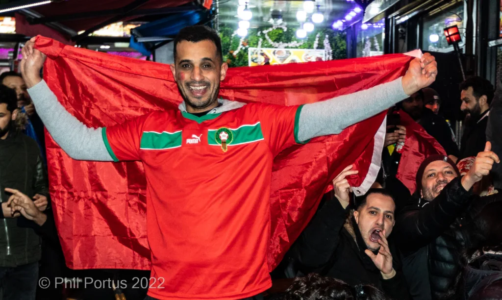 A man wearing a red jersey holds a large red cloth above his head amidst a crowd of people.
