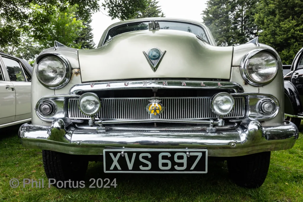 A vintage car with a chrome grill and headlights sits on green grass.