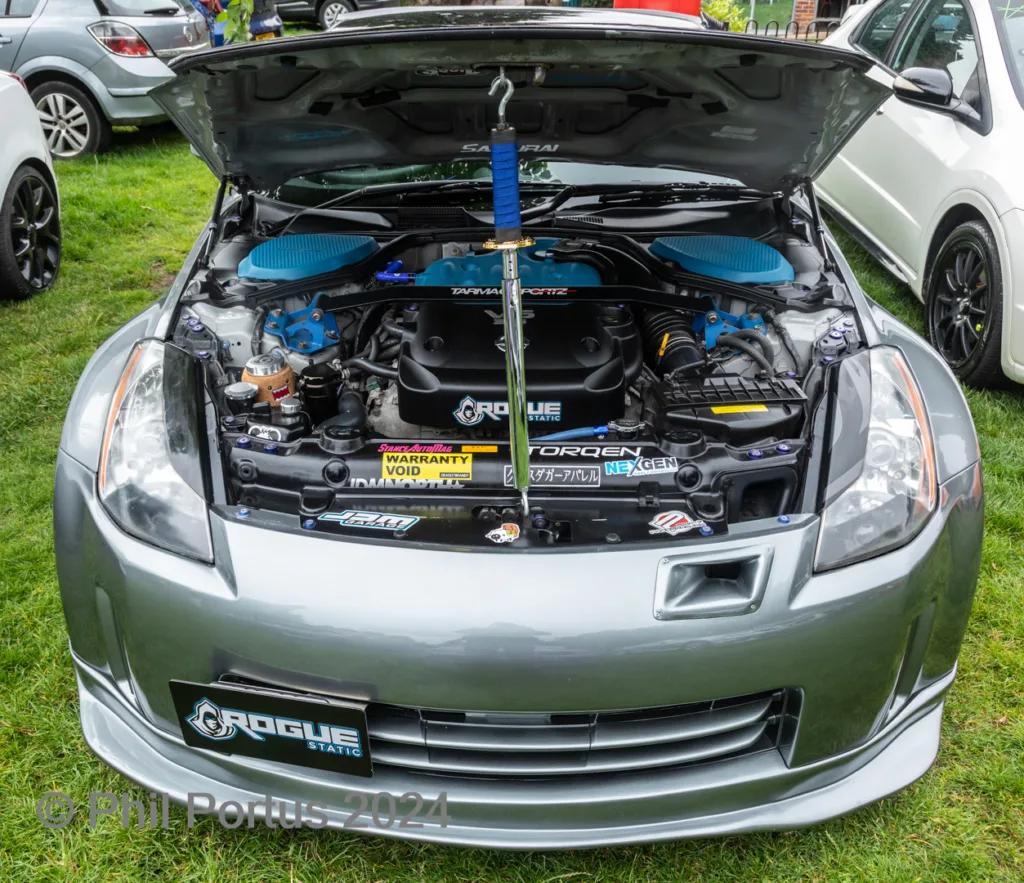 A silver car's engine bay is open, revealing a customized engine with blue and black components.