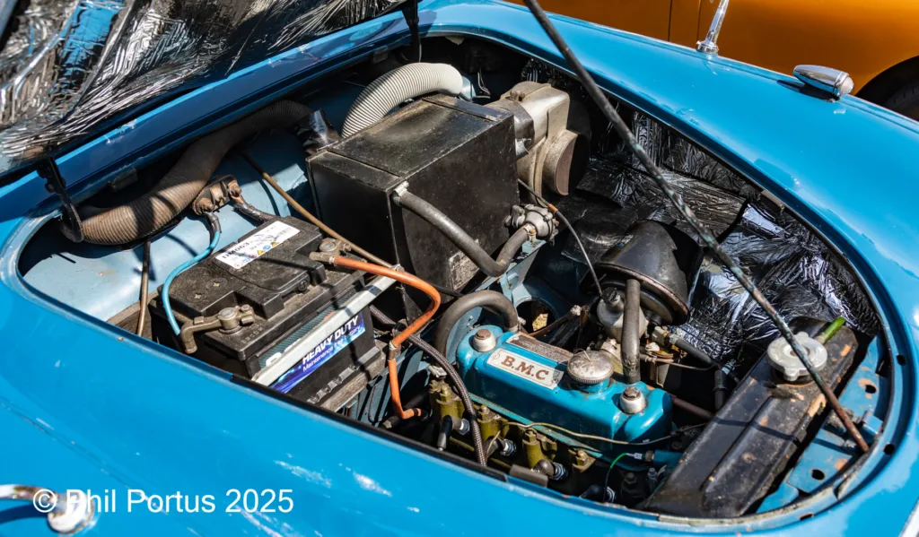 A vintage car's engine bay is visible under the open hood, showing various mechanical components.