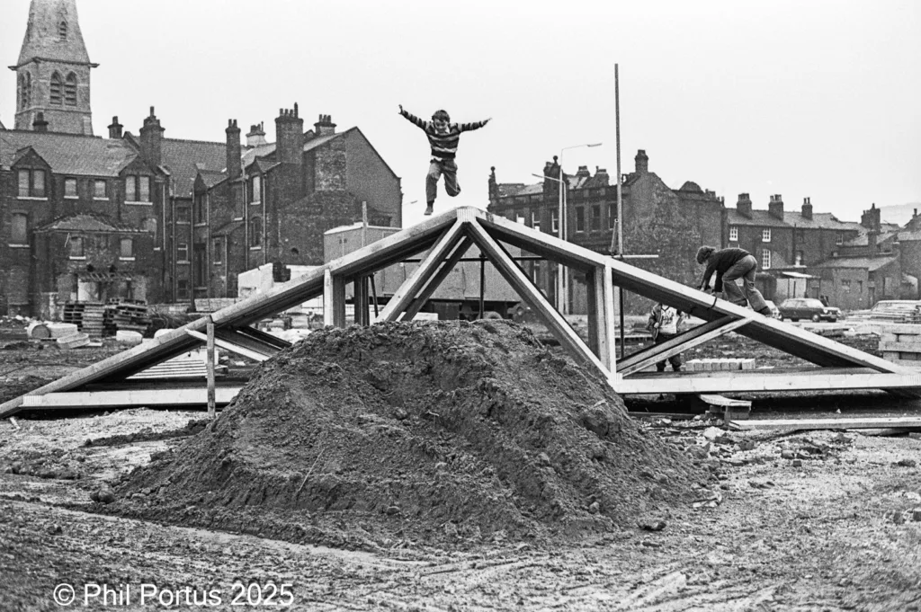 A black and white image shows a construction site with a wooden structure atop a mound of dirt.
